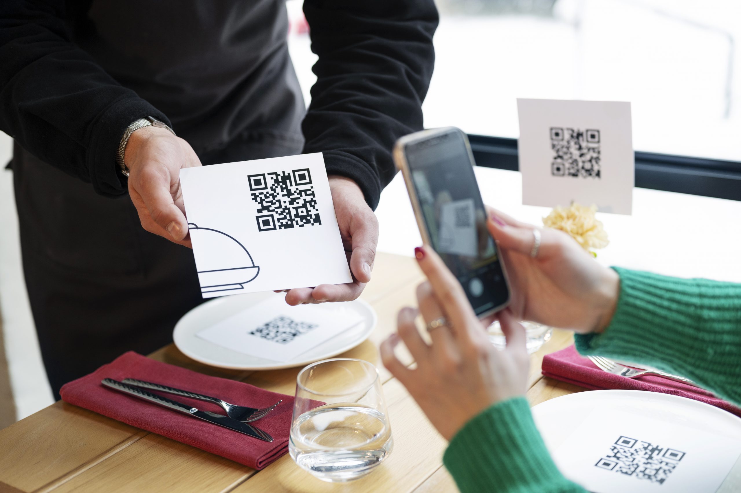 A waiter holding a qr code and a customer scan it with their camera.