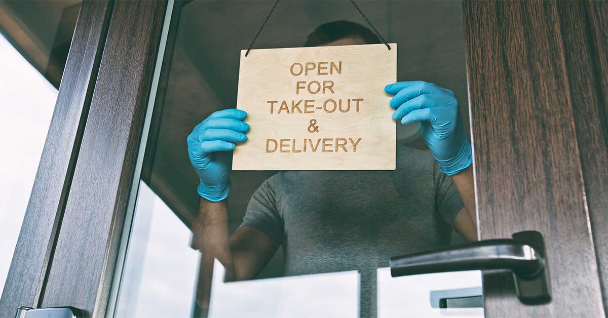man holds wooden sign with text open take out delivery